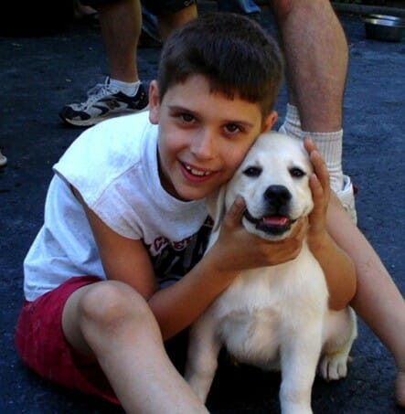 young boy sitting with a yellow lab puppy