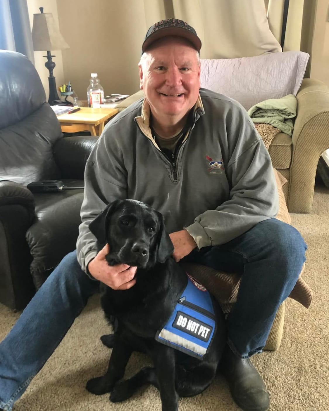 man sitting on a footstool in his living room with his black service dog